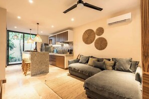 A modern living room with a sofa, a dining area with chairs, a kitchen with cabinets, and a ceiling fan. - Gem in the Jungle Private Pool Beach Club Access (Tulum)
