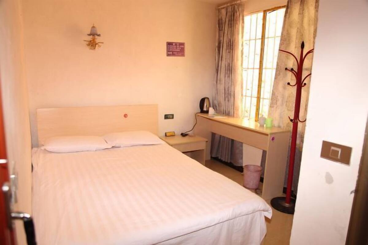 A bedroom with a bed, a desk, a chair, a lamp, and a window with curtains.