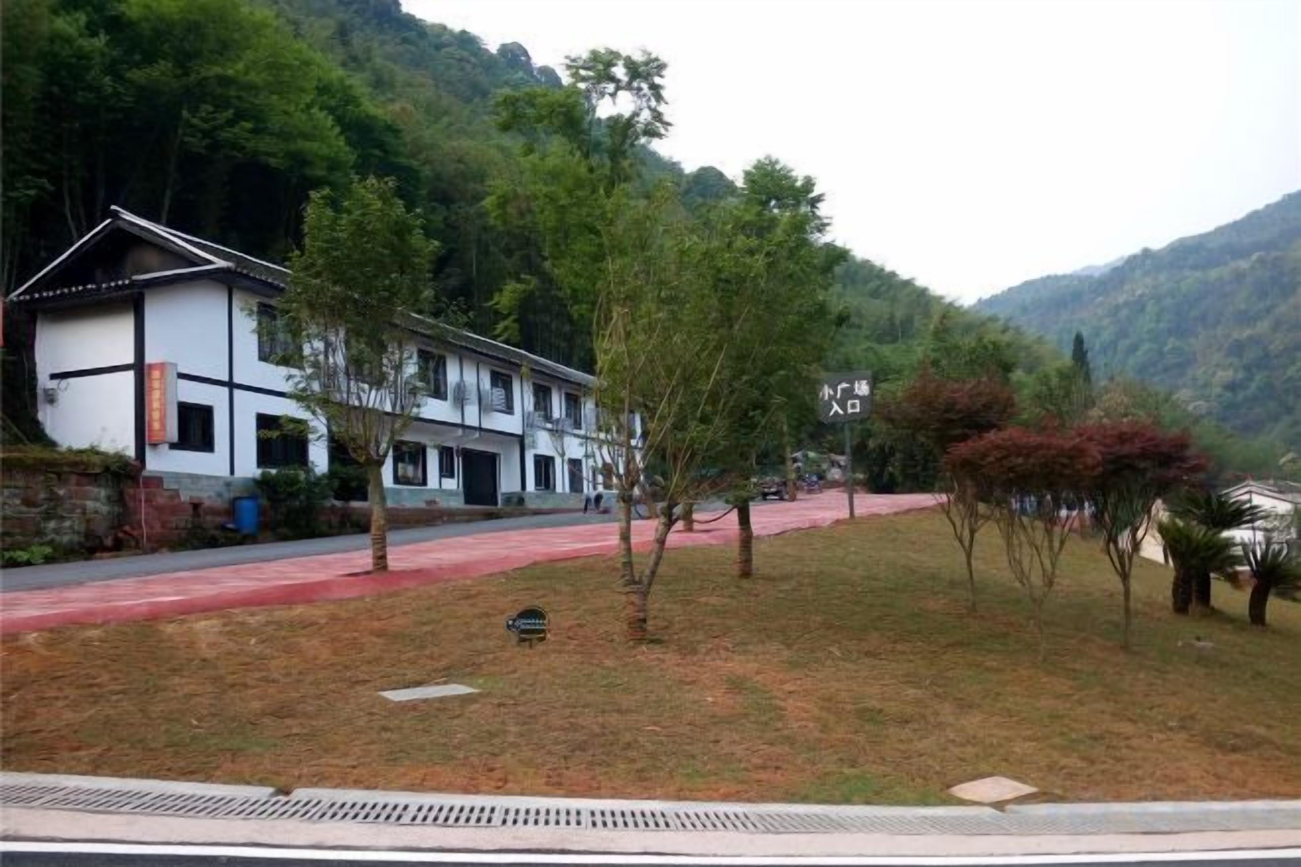 A traditional building with a red pathway leading to it, surrounded by trees and hills.