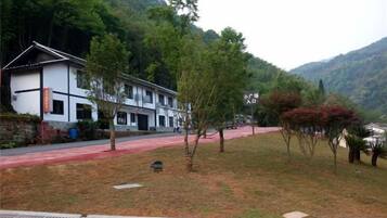 A traditional building with a red pathway leading to it, surrounded by trees and hills.