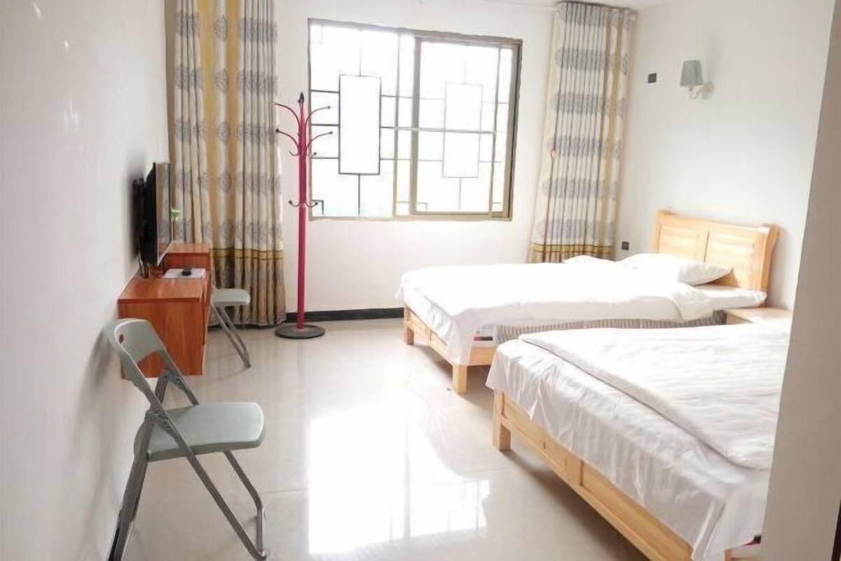 A hotel room with two beds, a desk, a chair, a TV, and a window with curtains.