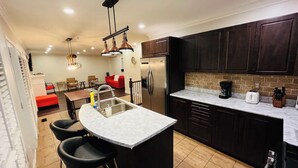 A modern kitchen with dark cabinets, a central island with bar stools, a stainless steel sink, and a refrigerator. - Spacious & Elegant 3BR + Office (Brantford)