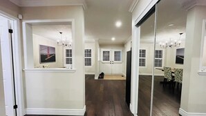 A spacious hallway with dark wooden flooring, white walls, and a large sliding glass door leading to a dining area with a table and chairs. - Spacious & Elegant 3BR + Office (Brantford)