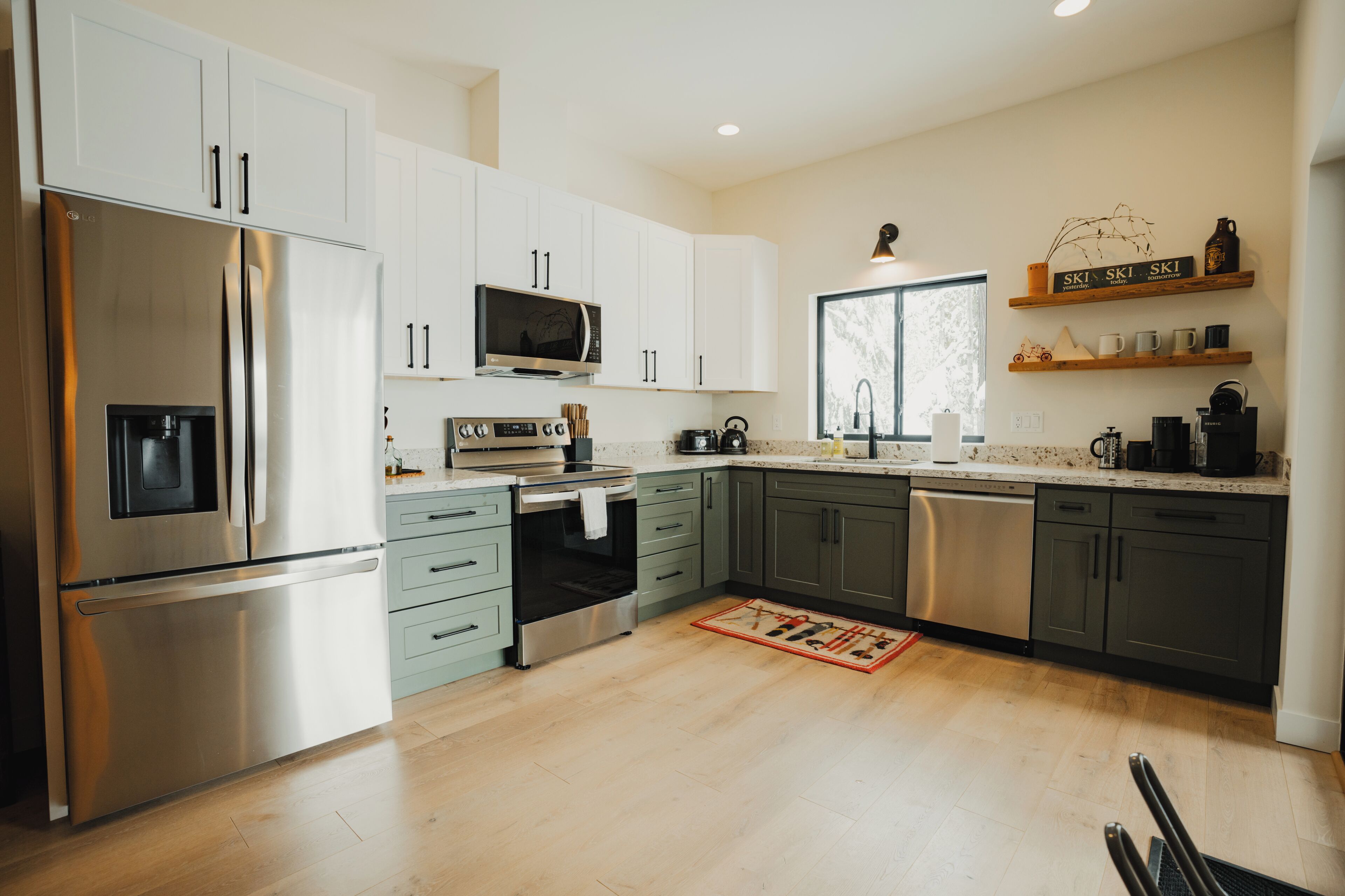 Una cucina moderna con elettrodomestici in acciaio inossidabile, mobili bianchi e pavimento in legno.