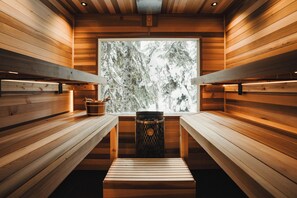 Un sauna avec des bancs en bois, une fenêtre donnant sur une forêt enneigée et une poubelle.