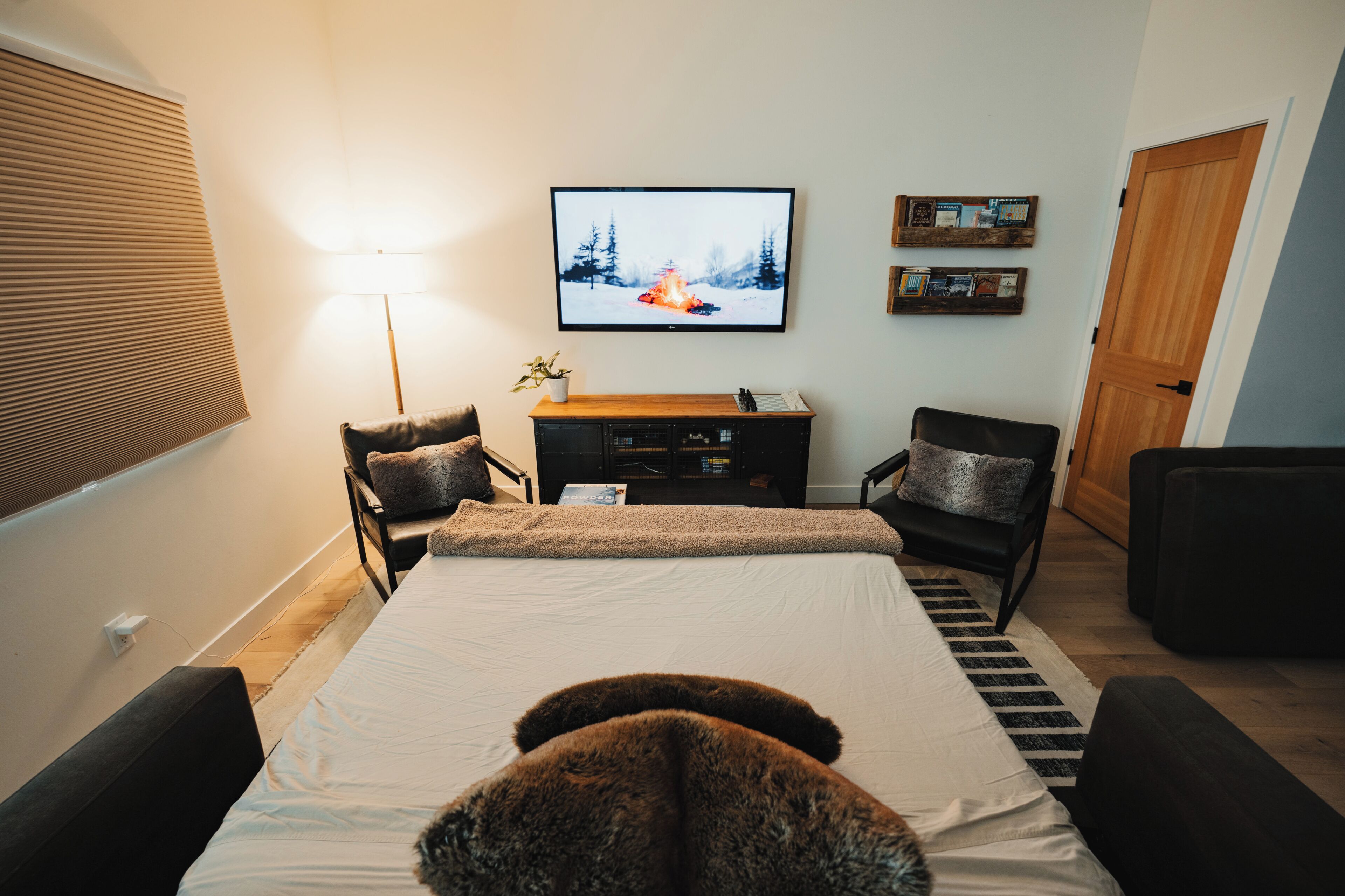 A bedroom with a bed, two chairs, a TV, a lamp, and a bookshelf.