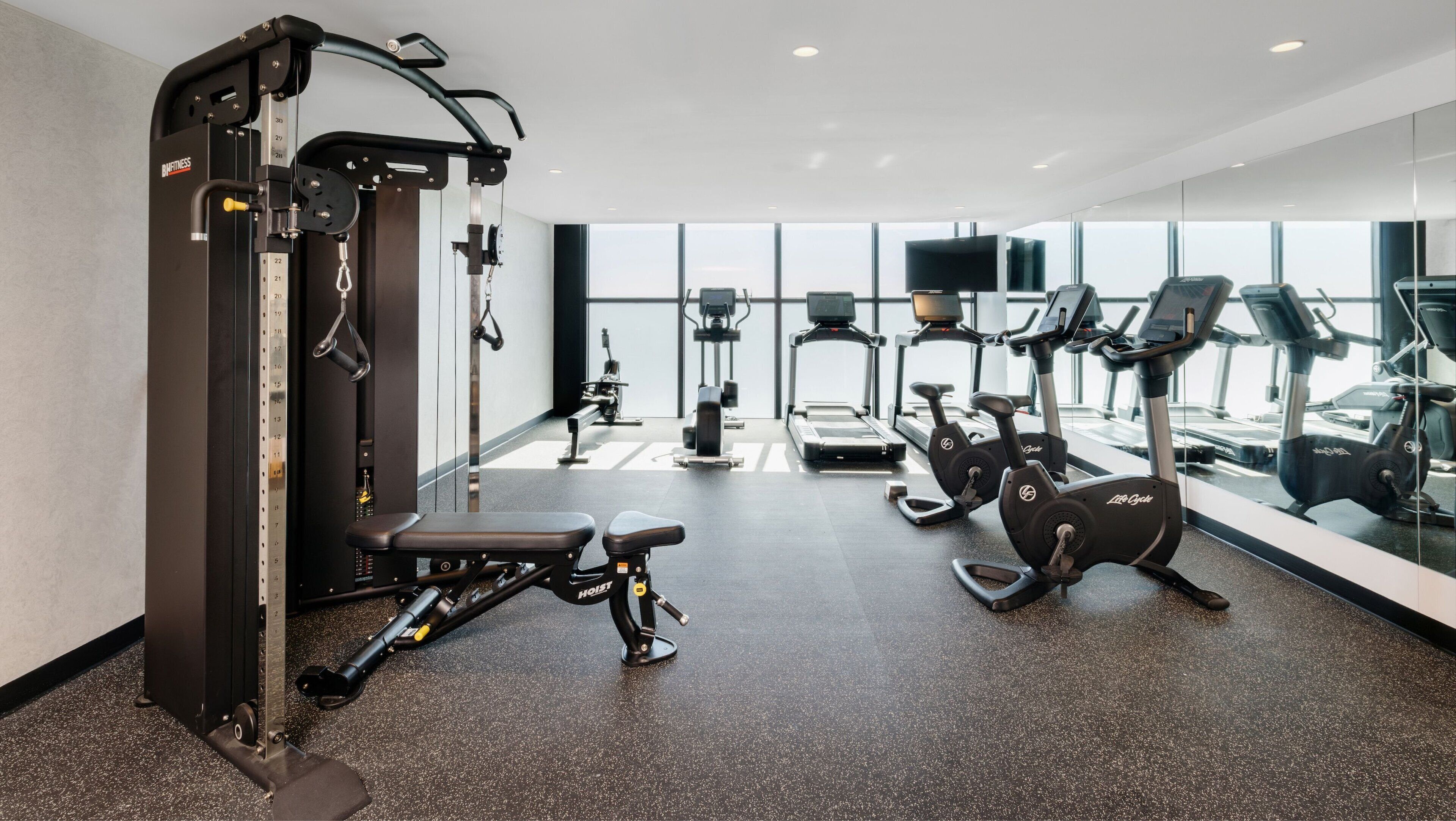 A modern gym with various exercise equipment, including a Smith machine, treadmills, and elliptical machines.