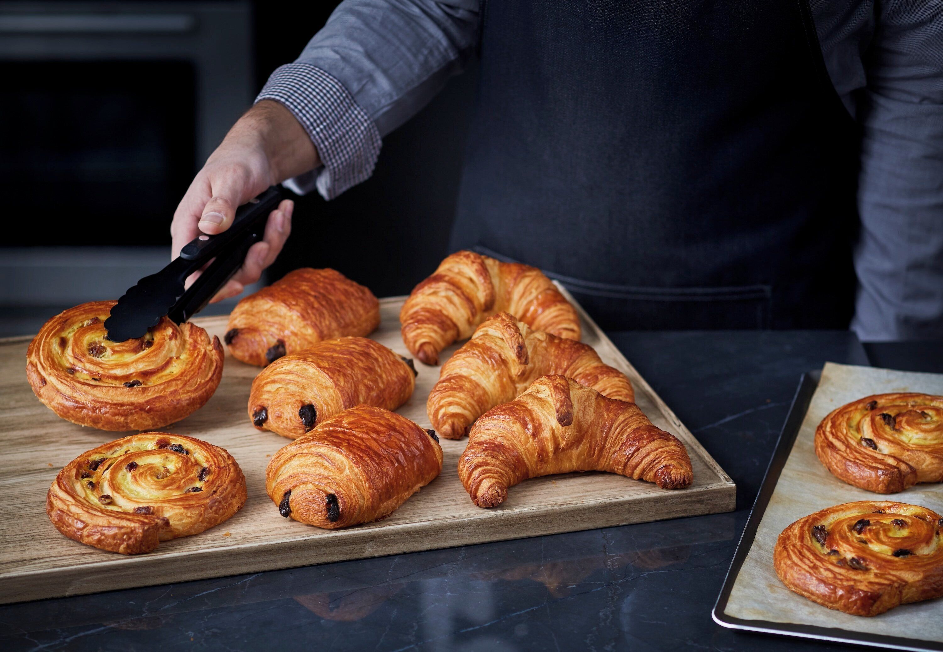 A person cutting a croissant on a wooden cutting board.