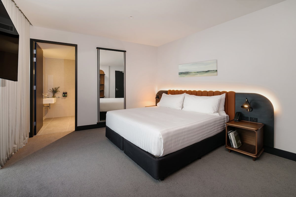 Ein modernes Schlafzimmer mit einem großen Bett, einem Nachttisch mit Büchern, einer Wandlampe und einem Gemälde über dem Bett.