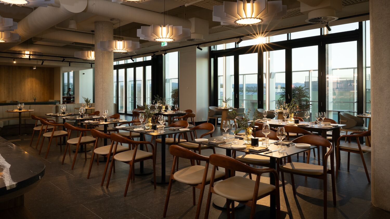 A restaurant with multiple tables set for dining, large windows, and modern lighting fixtures.