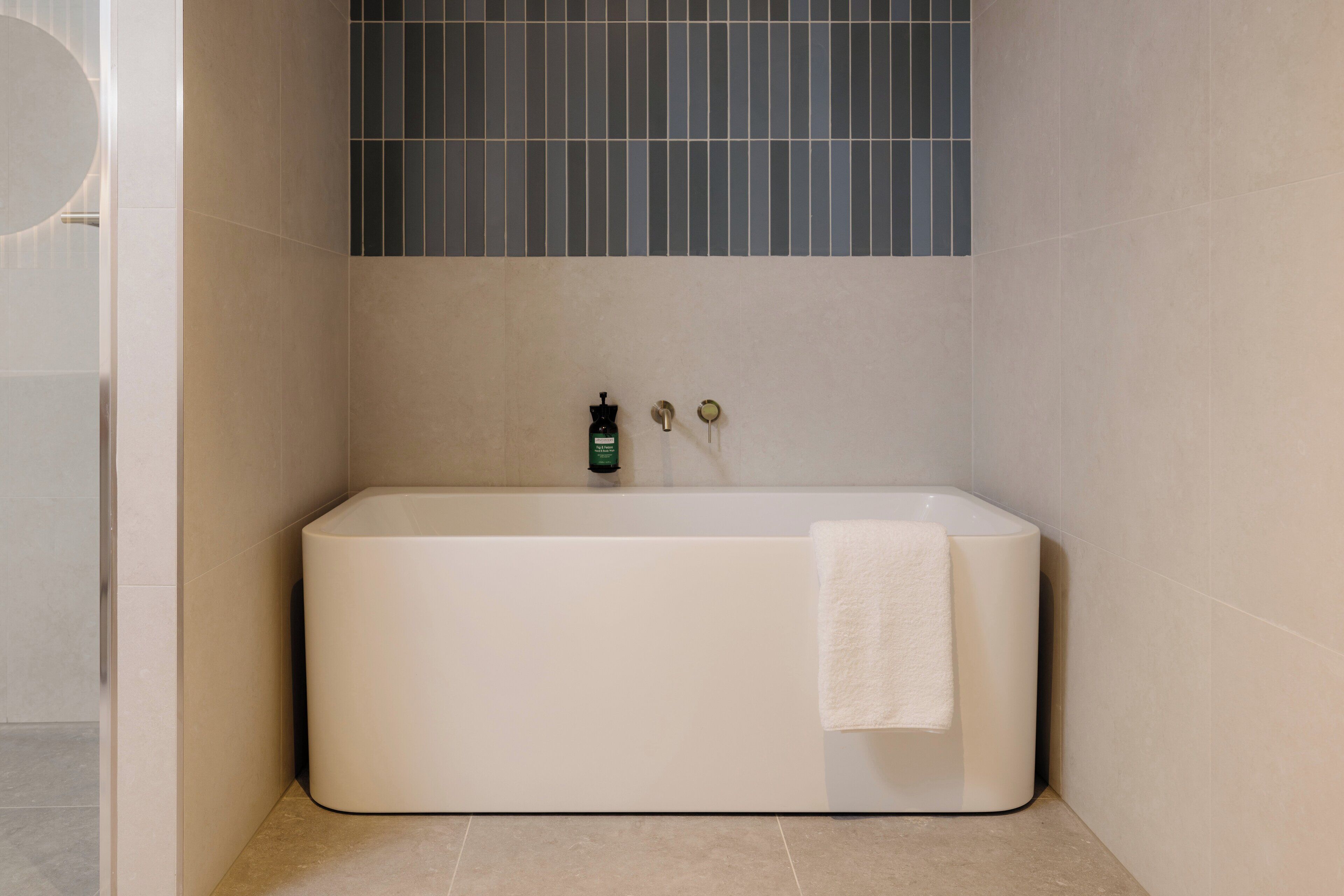 A modern bathroom with a freestanding bathtub, a towel hanging on the side, and a green bottle on the wall.