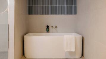 A modern bathroom with a freestanding bathtub, a towel hanging on the side, and a green bottle on the wall.