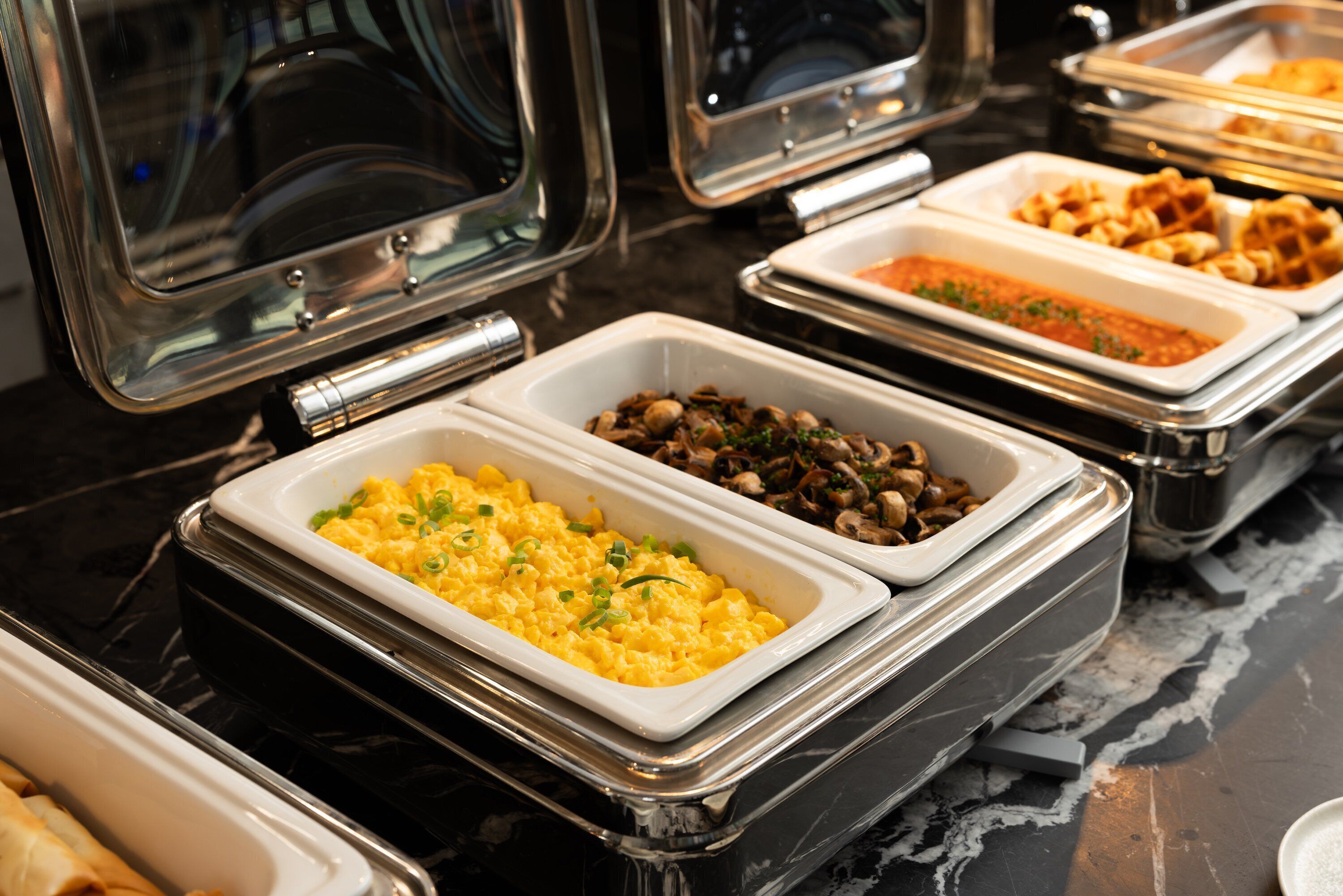 A buffet with various food options including scrambled eggs, mushrooms, and waffles.