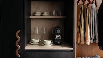 A dark wooden wardrobe with a curved handle, a shelf with cups and glasses, and a coffee maker.
