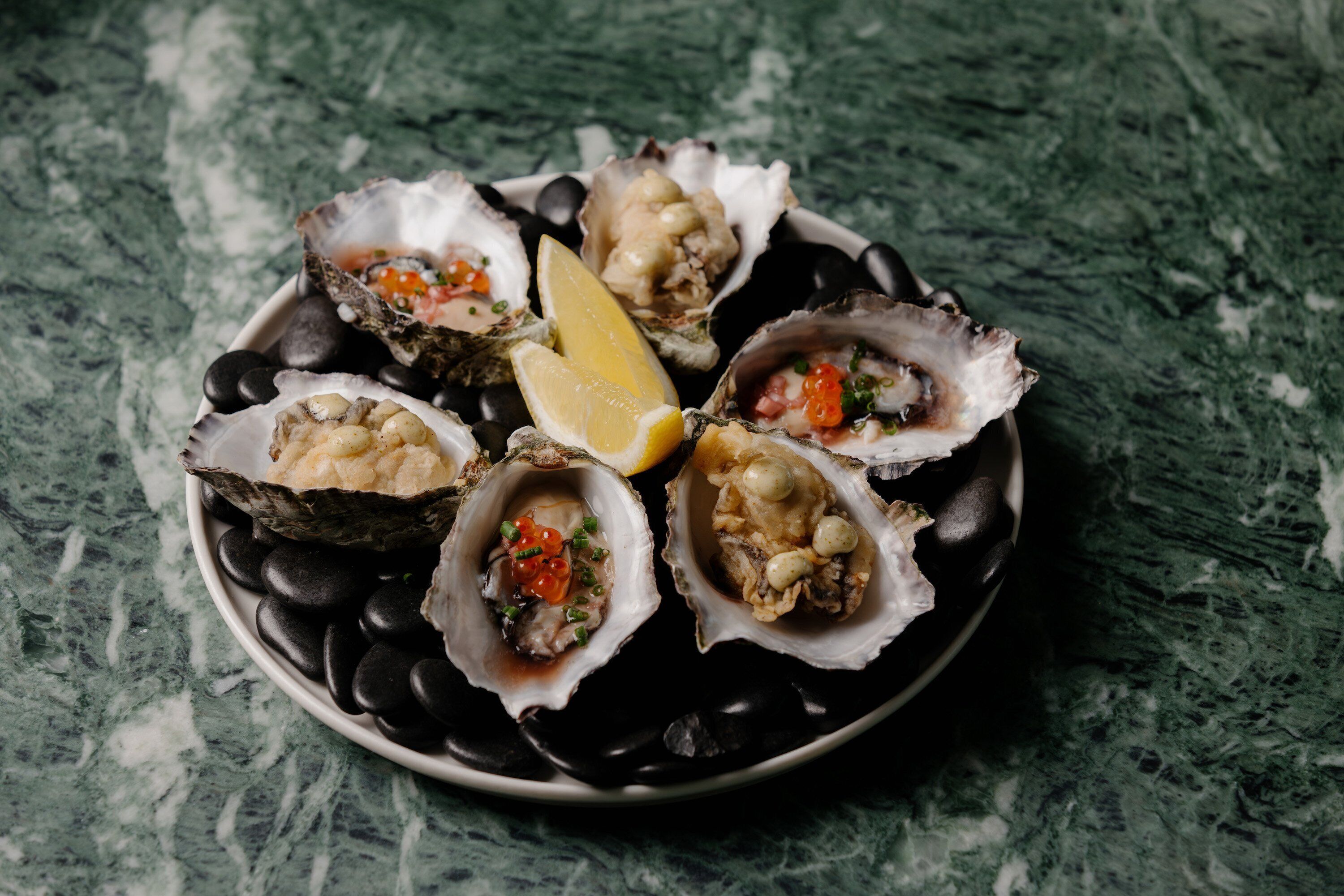 A plate of oysters with lemon wedges on a dark plate.