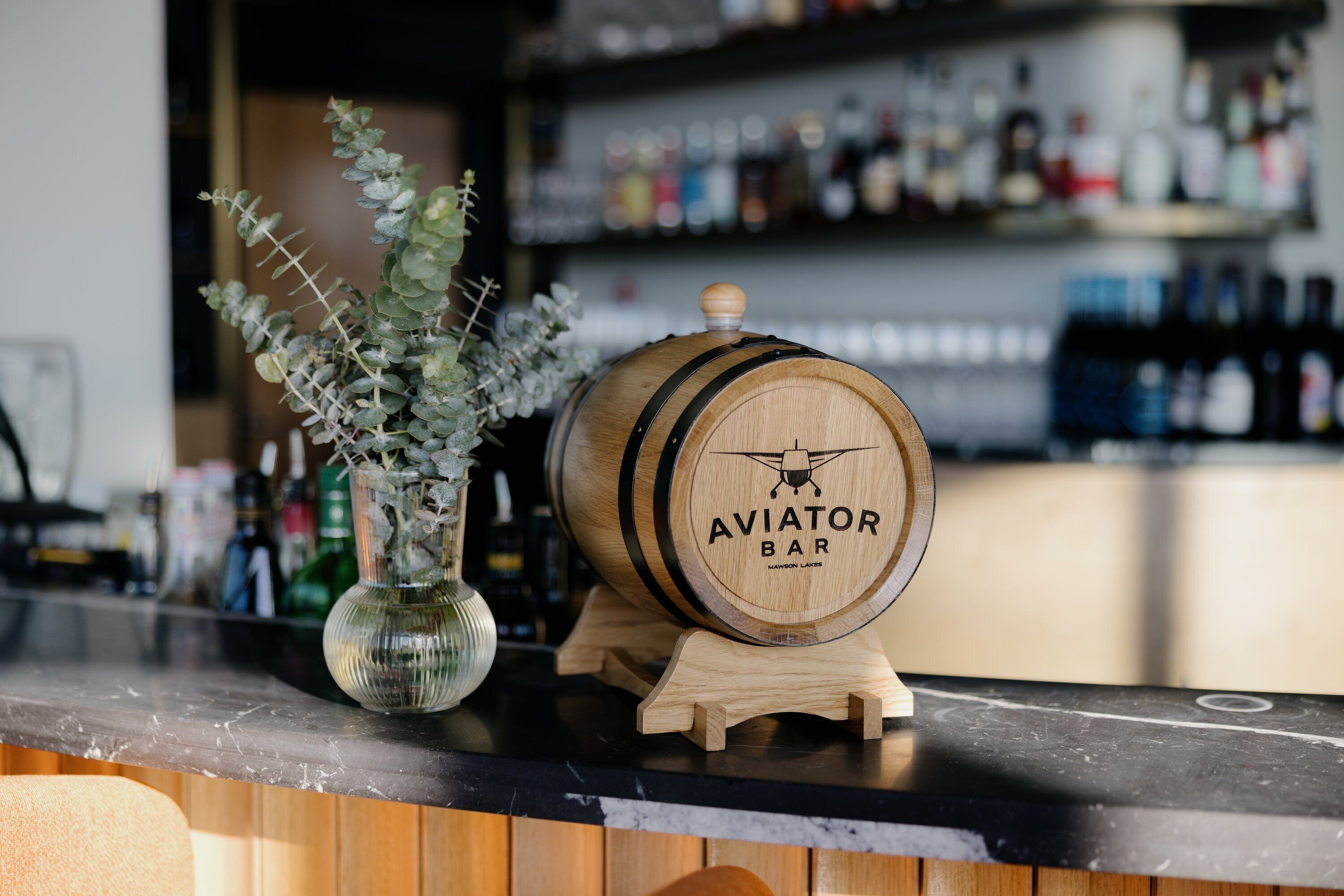 A wooden barrel with "AVIATOR BAR" on it, placed on a stand at a bar counter.