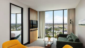 Une chambre d’hôtel moderne dotée d’une grande fenêtre, d’un téléviseur à écran plat, d’un canapé, d’une table basse et d’un lit offrant une vue sur la ville.