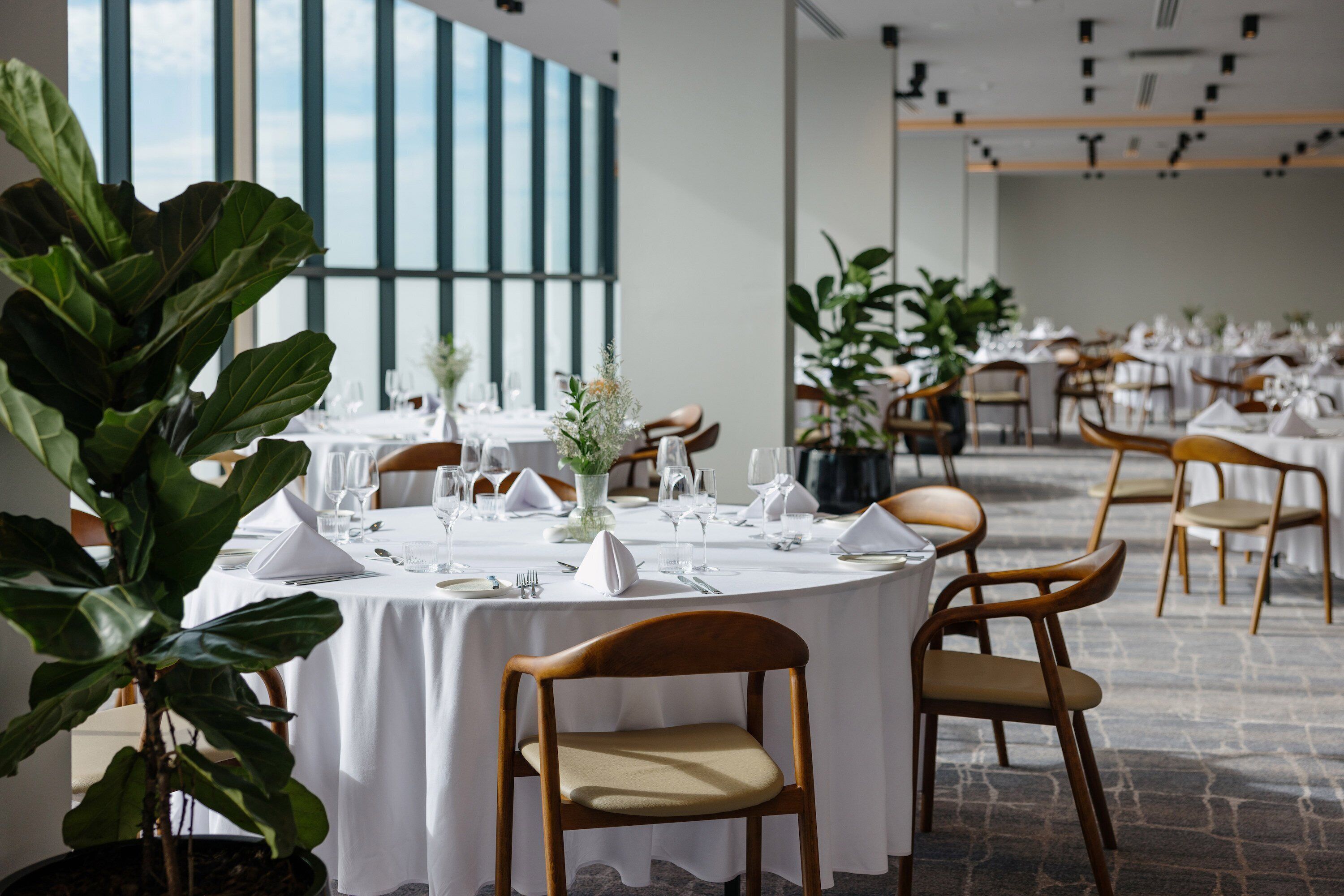 Un espace repas avec des tables rondes dressées pour le repas, entourées de chaises et de plantes en pot.