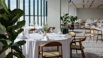 Un espace repas avec des tables rondes dressées pour le repas, entourées de chaises et de plantes en pot.