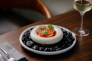 A dessert on a plate with black beans around it, a glass of white wine, and a napkin on the table. - Crowne Plaza Adelaide Mawson Lakes by IHG (Mawson Lakes)