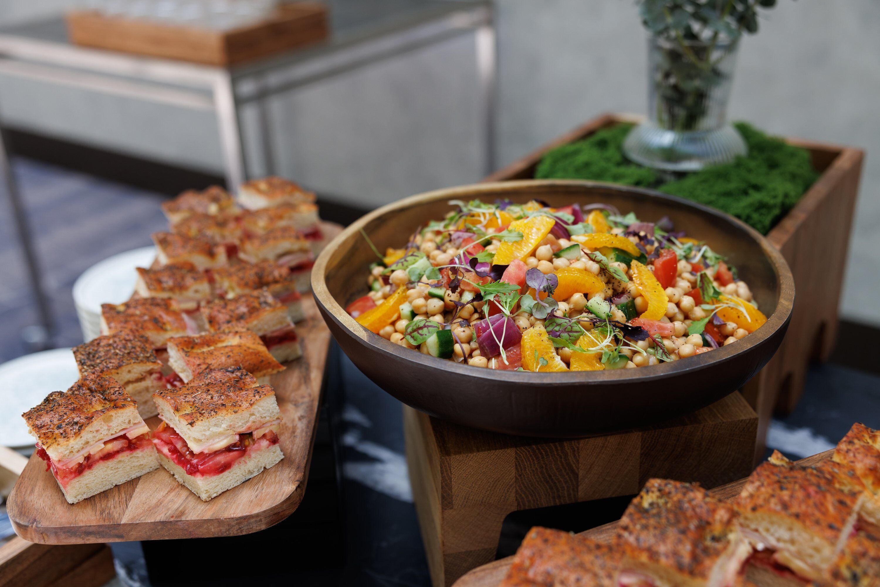 Une table de buffet proposant une variété de plats, notamment des sandwichs, une salade colorée et un bol de pois chiches.