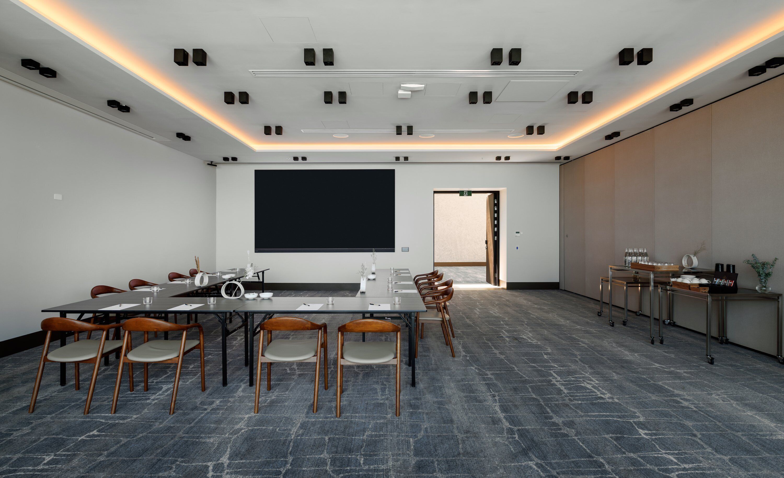A conference room with a large table, chairs, a projector screen, and a coffee station.