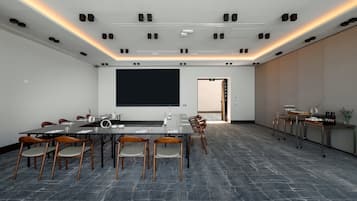 A conference room with a large table, chairs, a projector screen, and a coffee station.