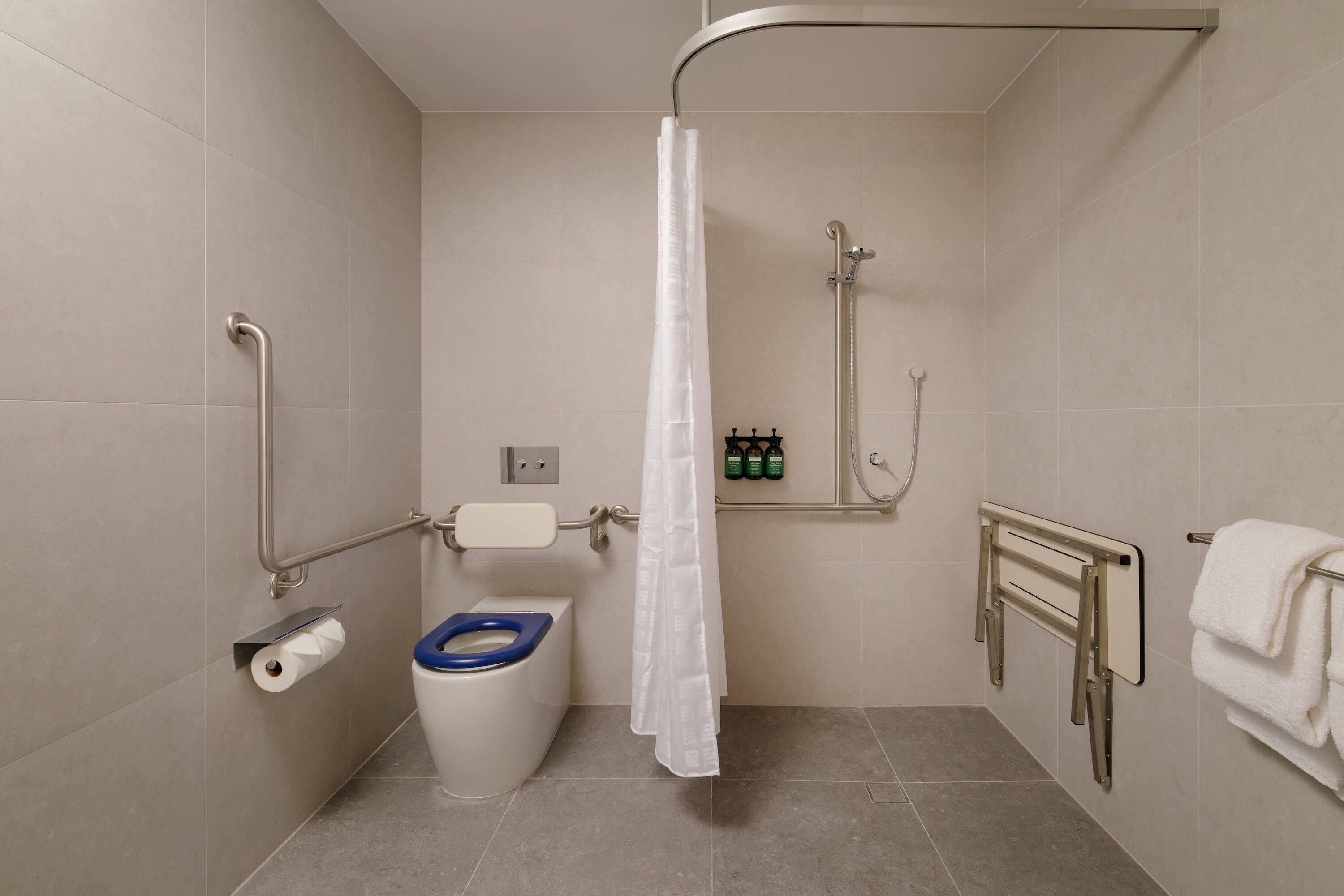 A bathroom with a toilet, shower, grab bars, and a towel rack.