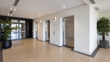 A modern hallway with a speckled floor, glass doors, and potted plants.