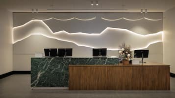 A reception desk with a marble top and wooden base, flanked by two monitors and a decorative plant.