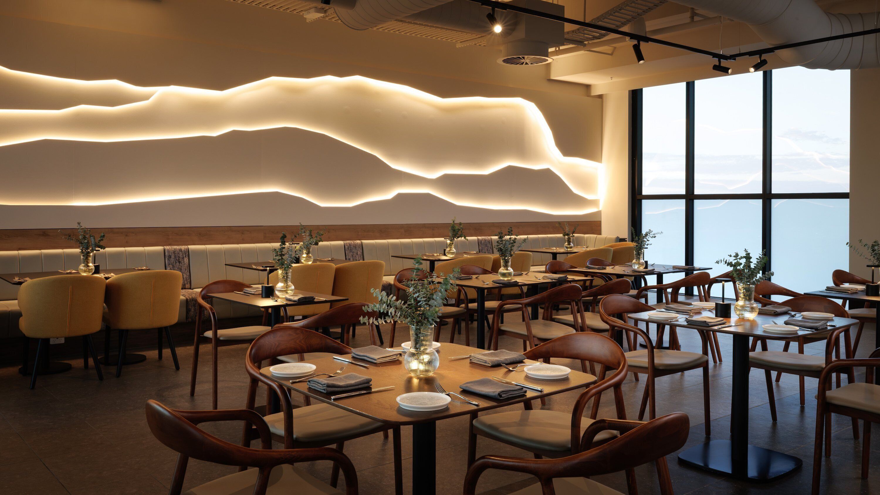 Un restaurante moderno con un diseño de techo único, muebles de madera y grandes ventanales que ofrecen una vista.