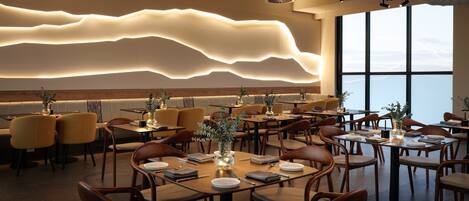 Ein modernes Restaurant mit einem einzigartigen Deckendesign, Holzmöbeln und großen Fenstern mit Blick.