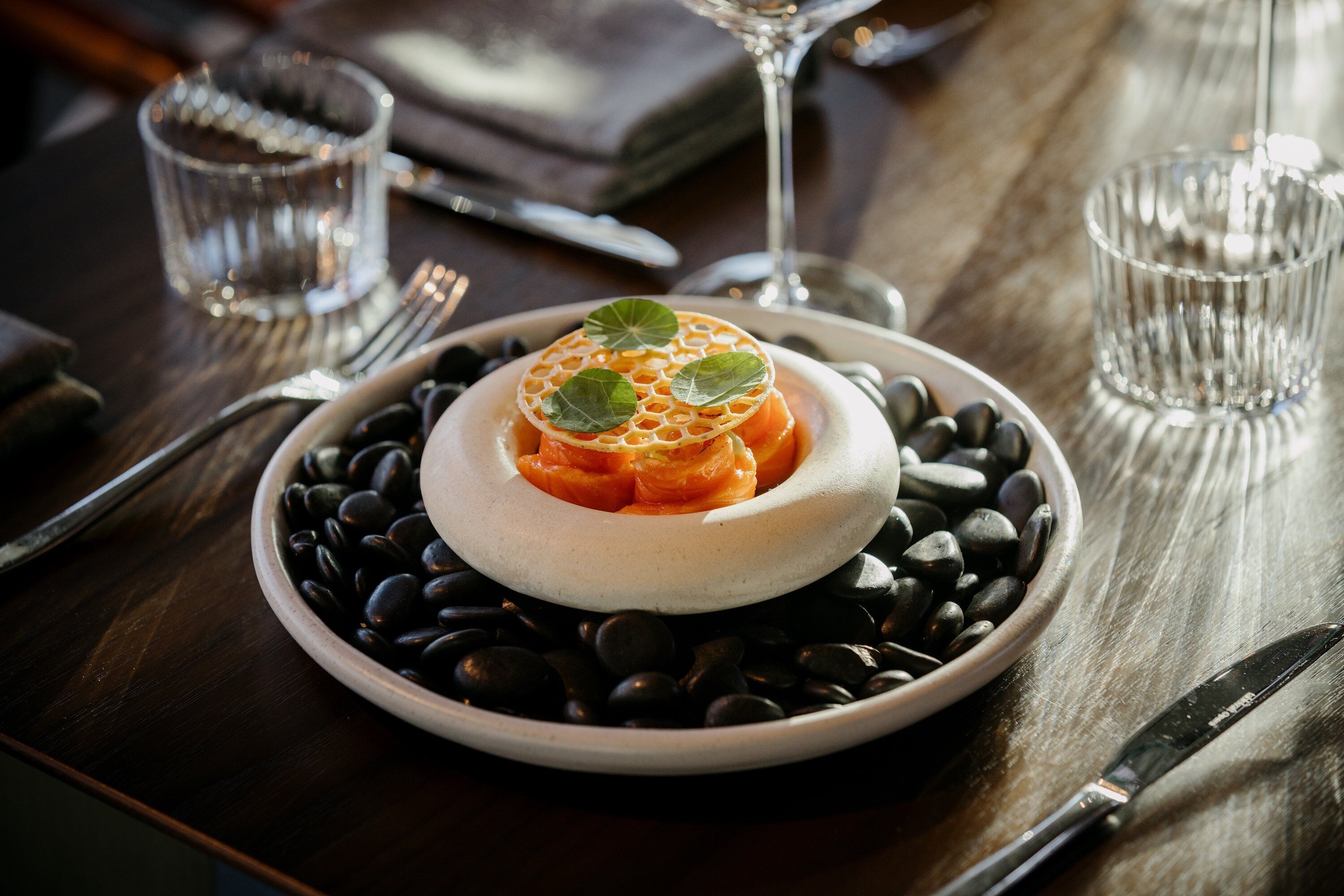 A dessert on a plate with black stones around it, placed on a wooden table.