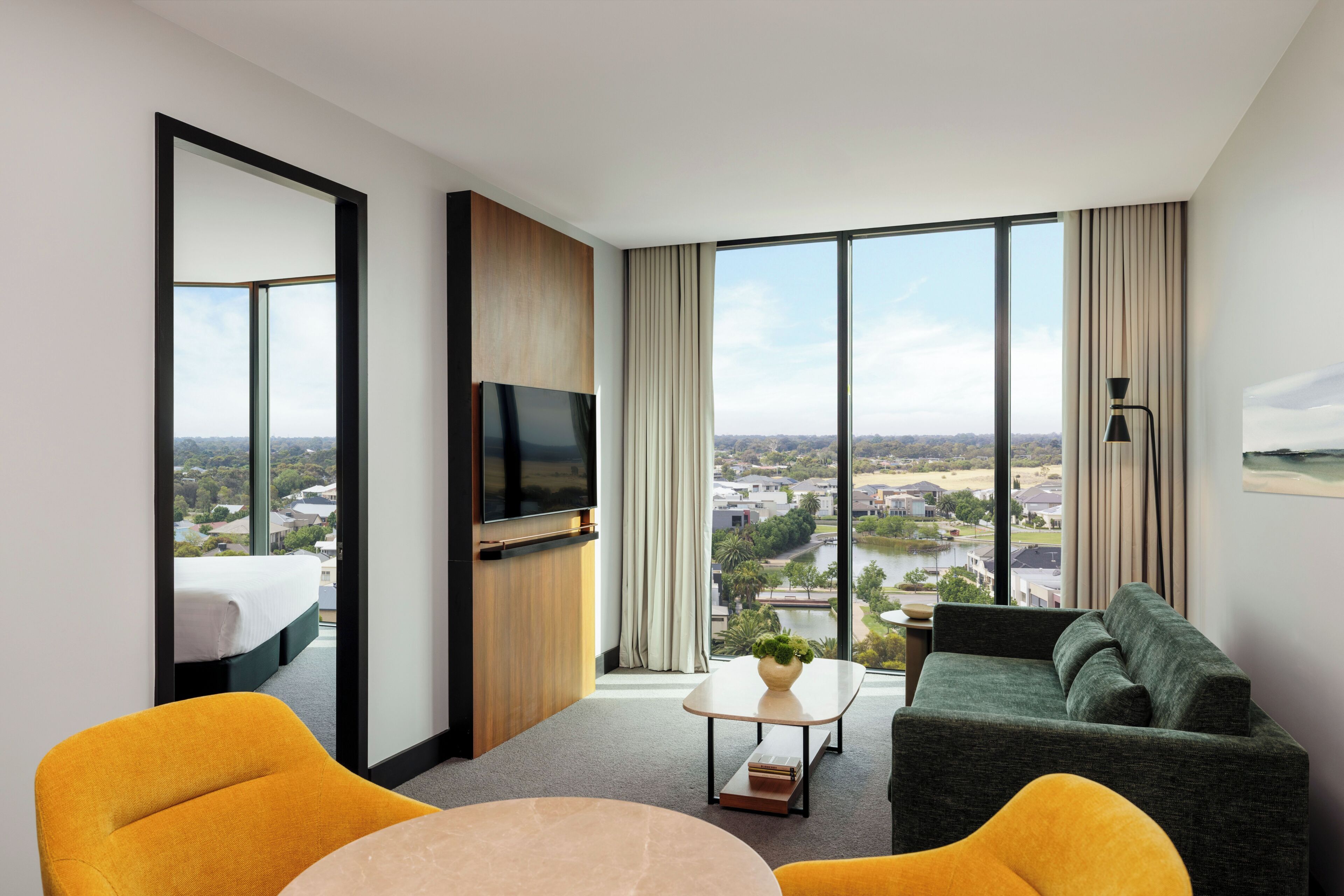 A modern hotel room with a bed, a TV, a sofa, and a dining table.