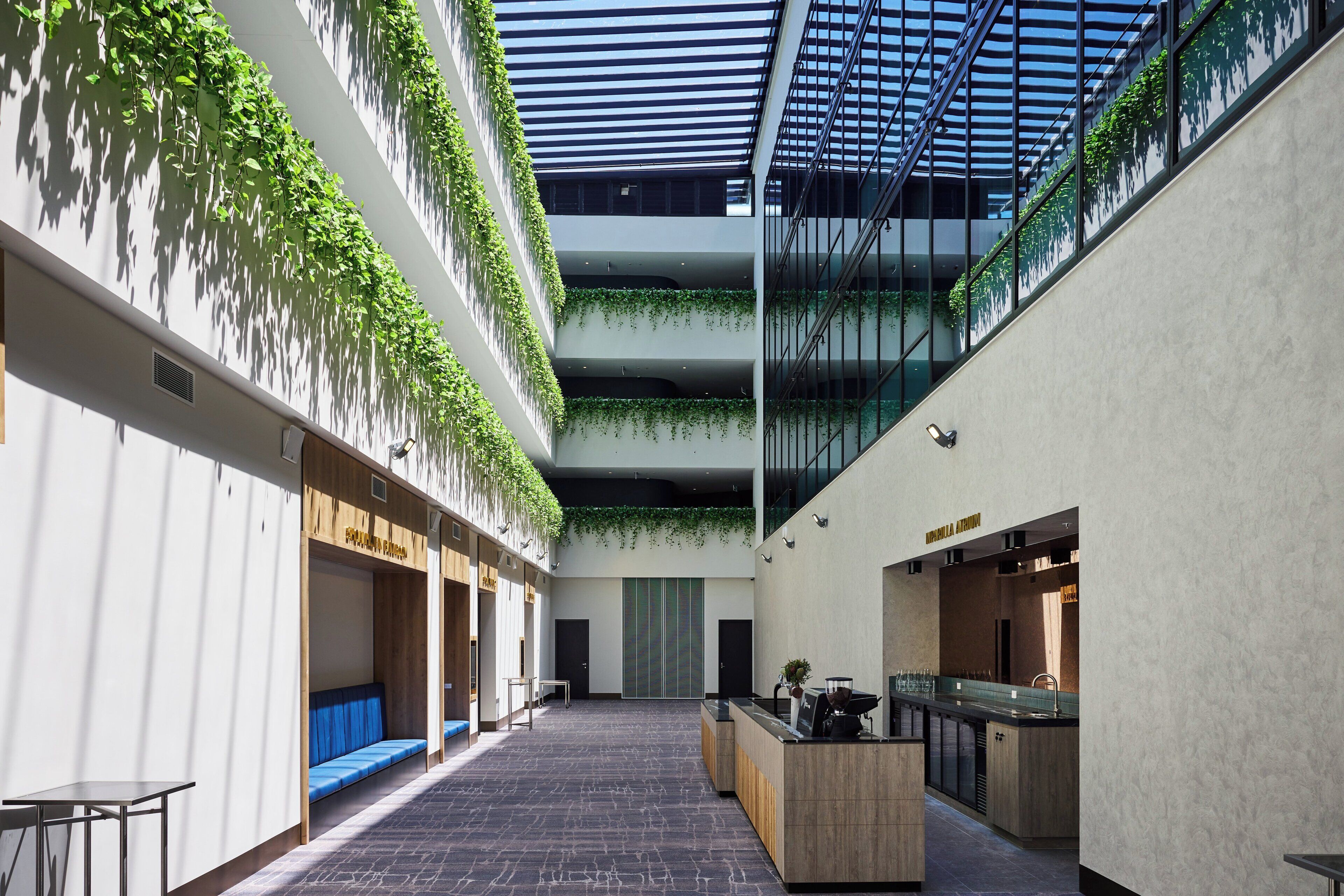 A modern interior with a central open space, wooden seating, a reception desk, and green plants on the walls.