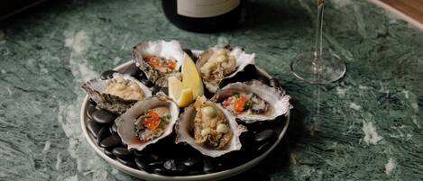 A plate of oysters with lemon and sauce, a bottle of champagne, and a glass of wine on a marble table.