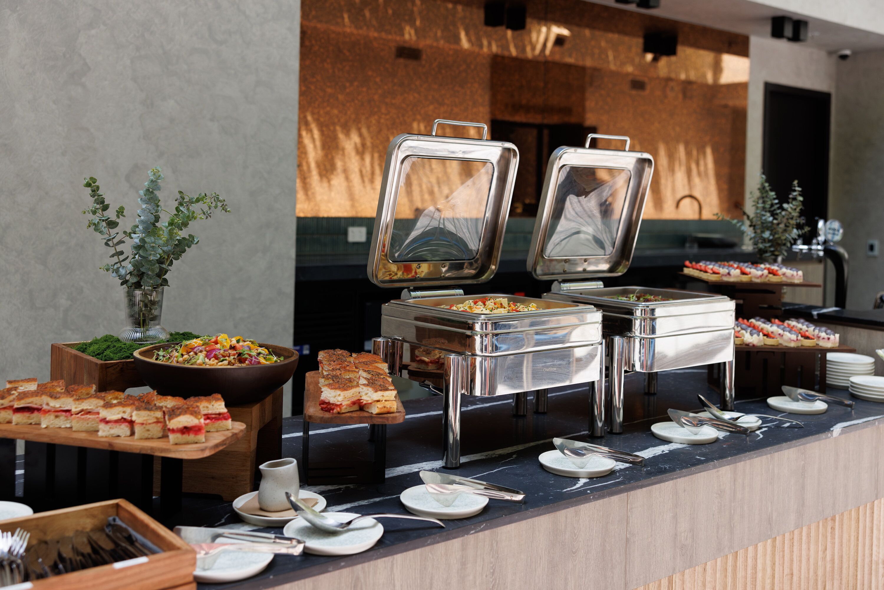 A buffet setup with various food items, including a salad, sandwiches, and a fruit display.