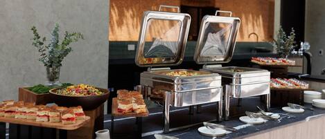 A buffet setup with various food items, including a salad, sandwiches, and a fruit display.
