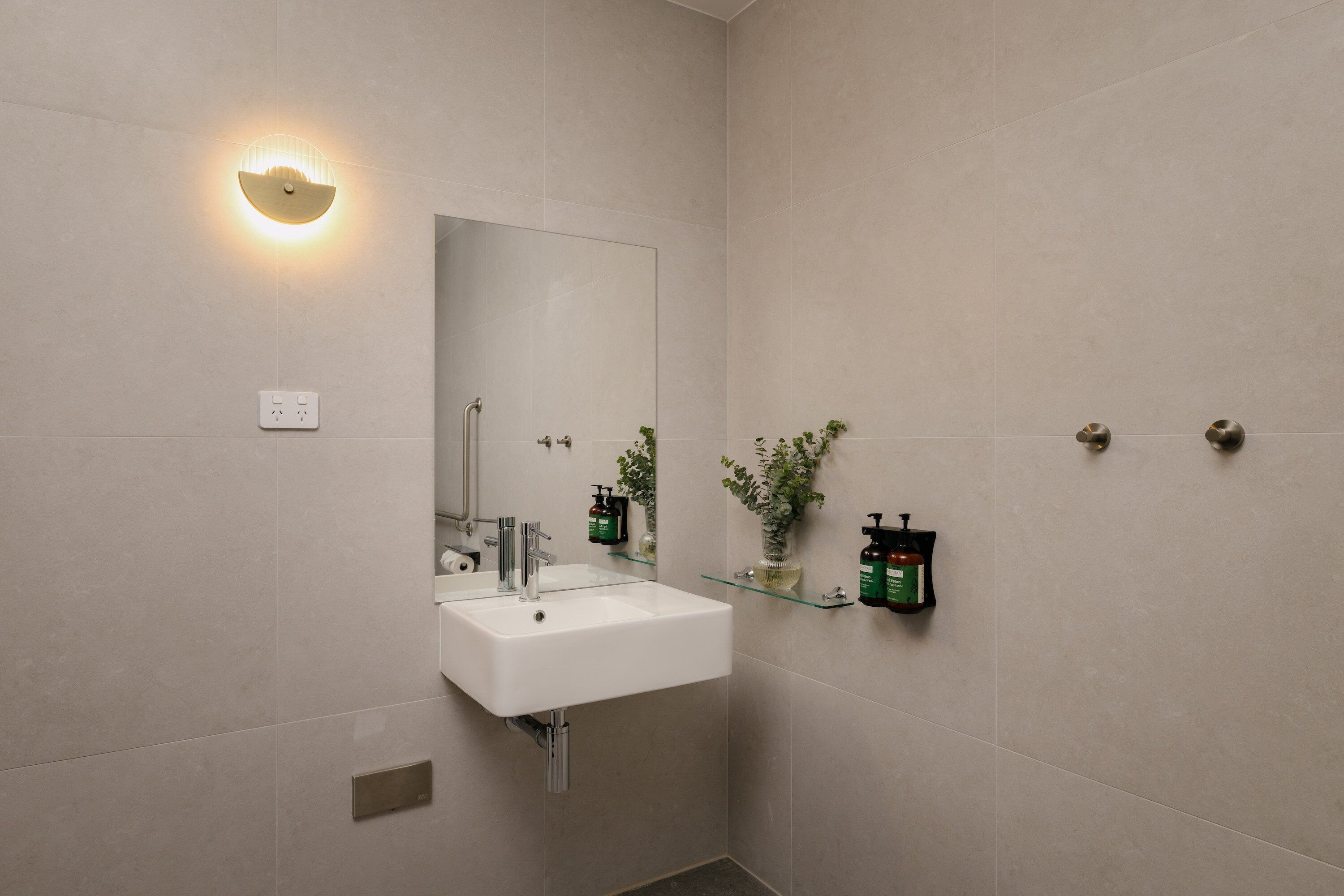 A modern bathroom with a white sink, mirror, and wall-mounted light fixture.