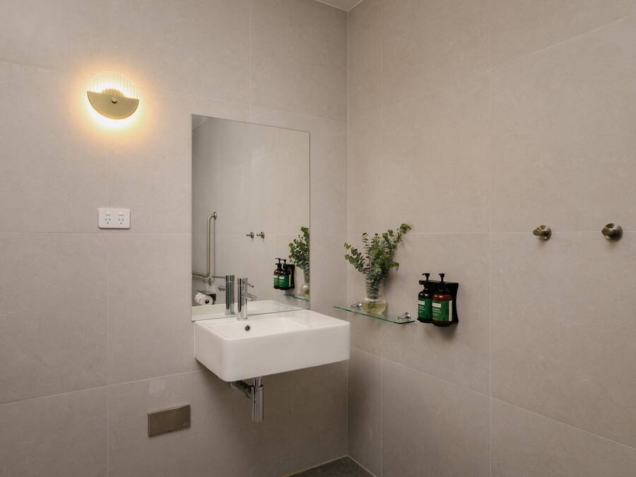A modern bathroom with a white sink, mirror, and wall-mounted light fixture.