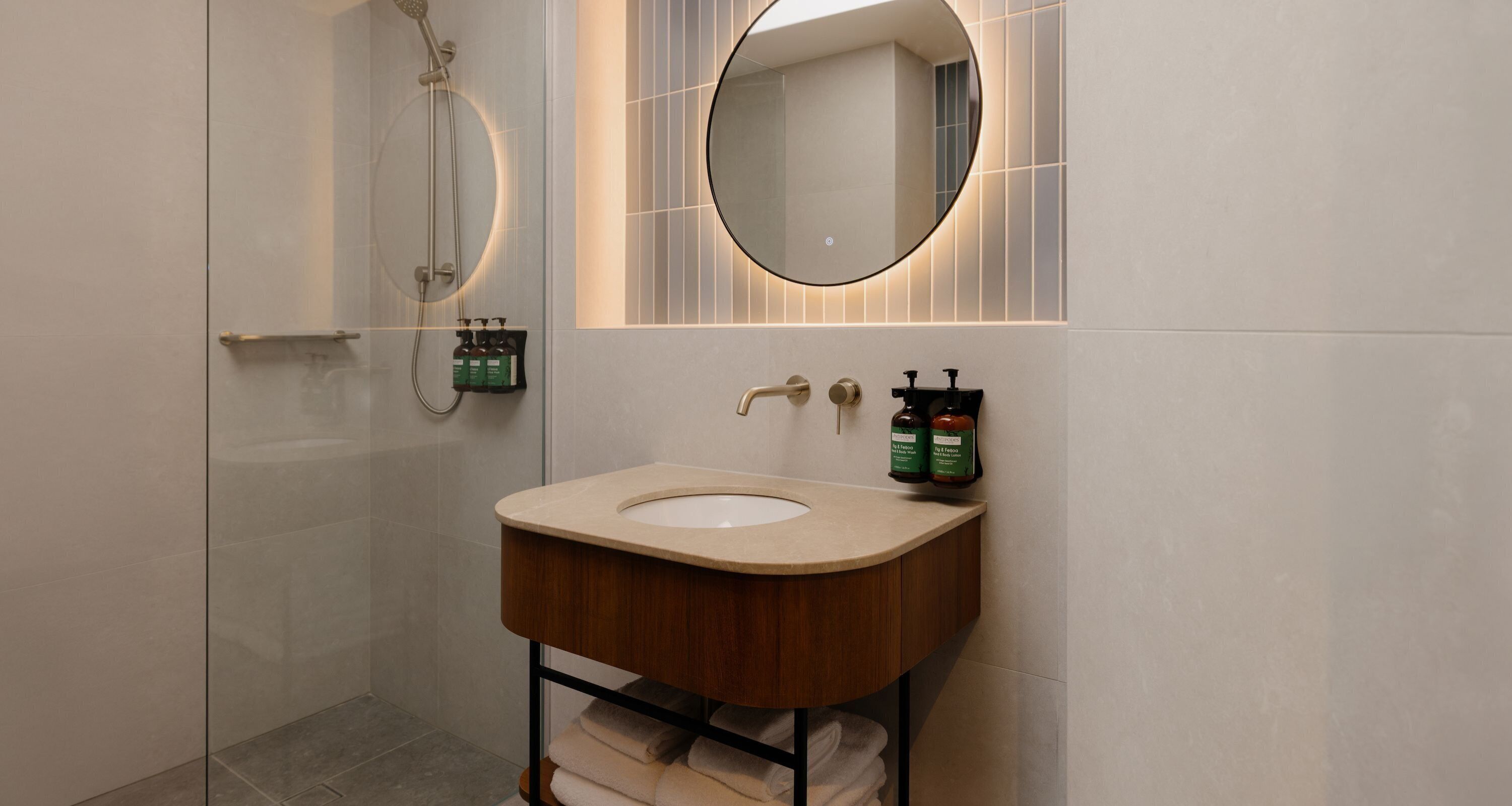A modern bathroom with a curved sink, a handheld showerhead, and a large mirror.