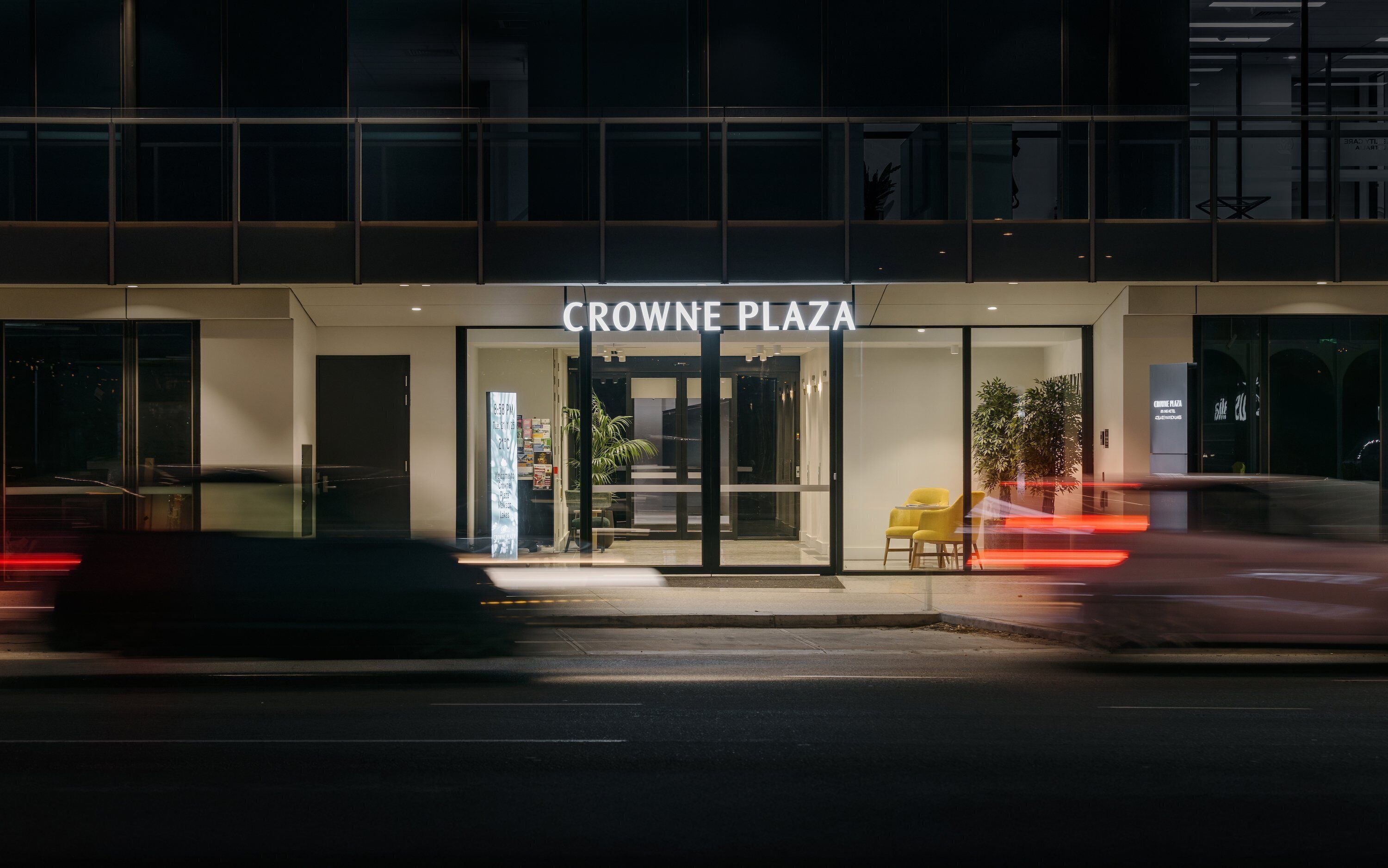 L’extérieur de l’hôtel Crowne Plaza se caractérise par une façade en verre, un panneau indicateur et une chaise jaune placée à l’extérieur.