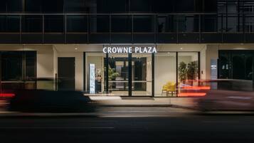 L’extérieur de l’hôtel Crowne Plaza se caractérise par une façade en verre, un panneau indicateur et une chaise jaune placée à l’extérieur.