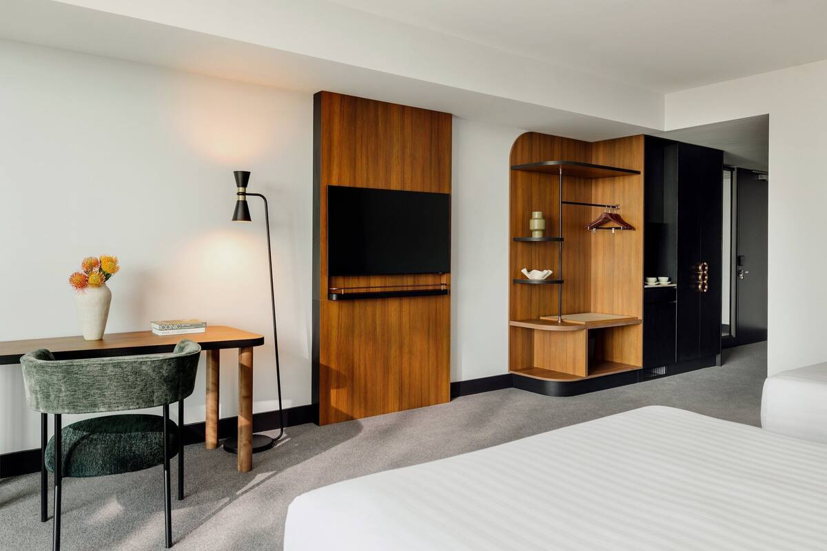 Ein Hotelzimmer mit Bett, Schreibtisch mit Stuhl, Fernseher, Kleiderschrank und einer kleinen Ablage mit Kleiderhaken.
