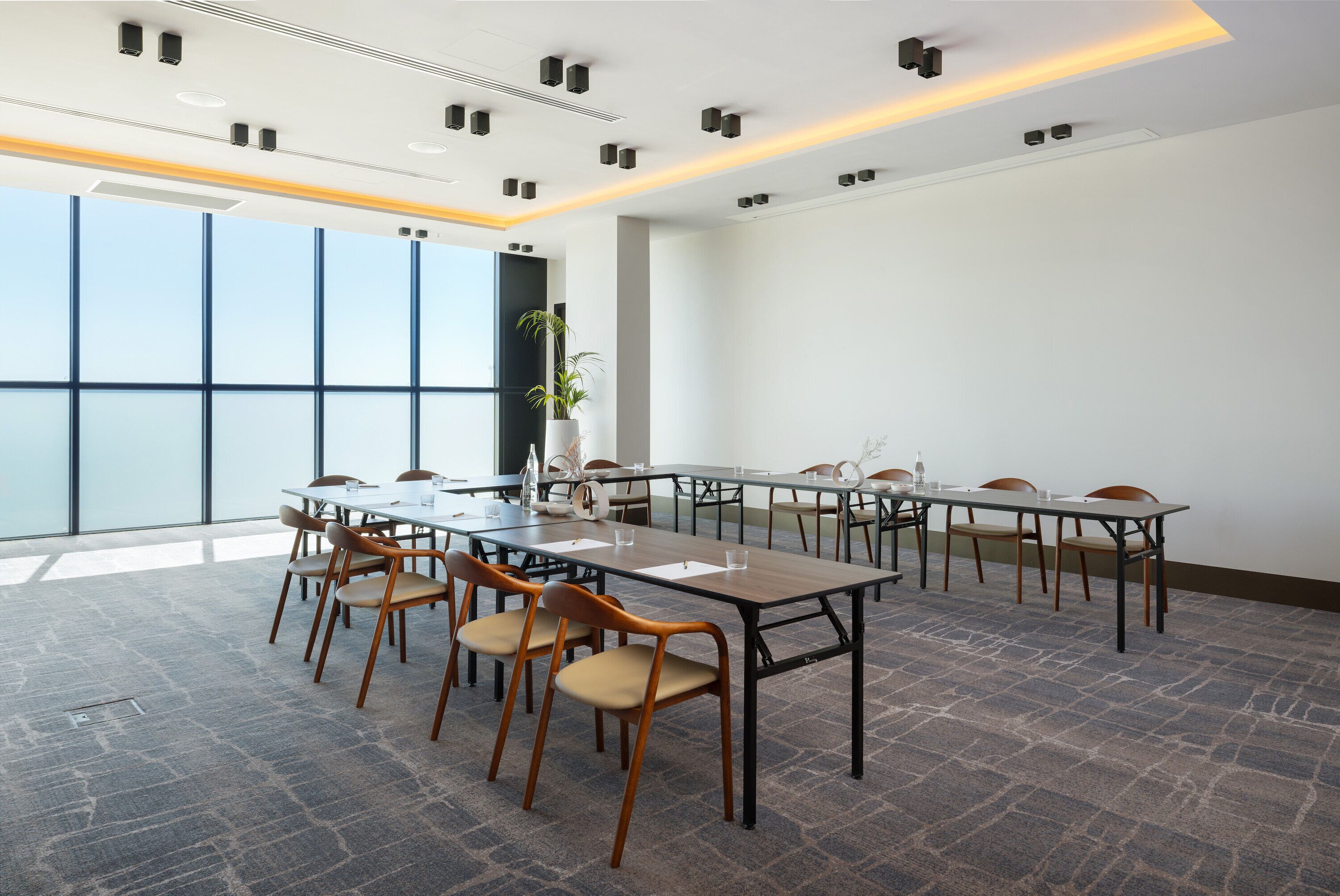 Un salón de conferencias con una larga mesa, varias sillas y un amplio ventanal que proporciona luz natural.