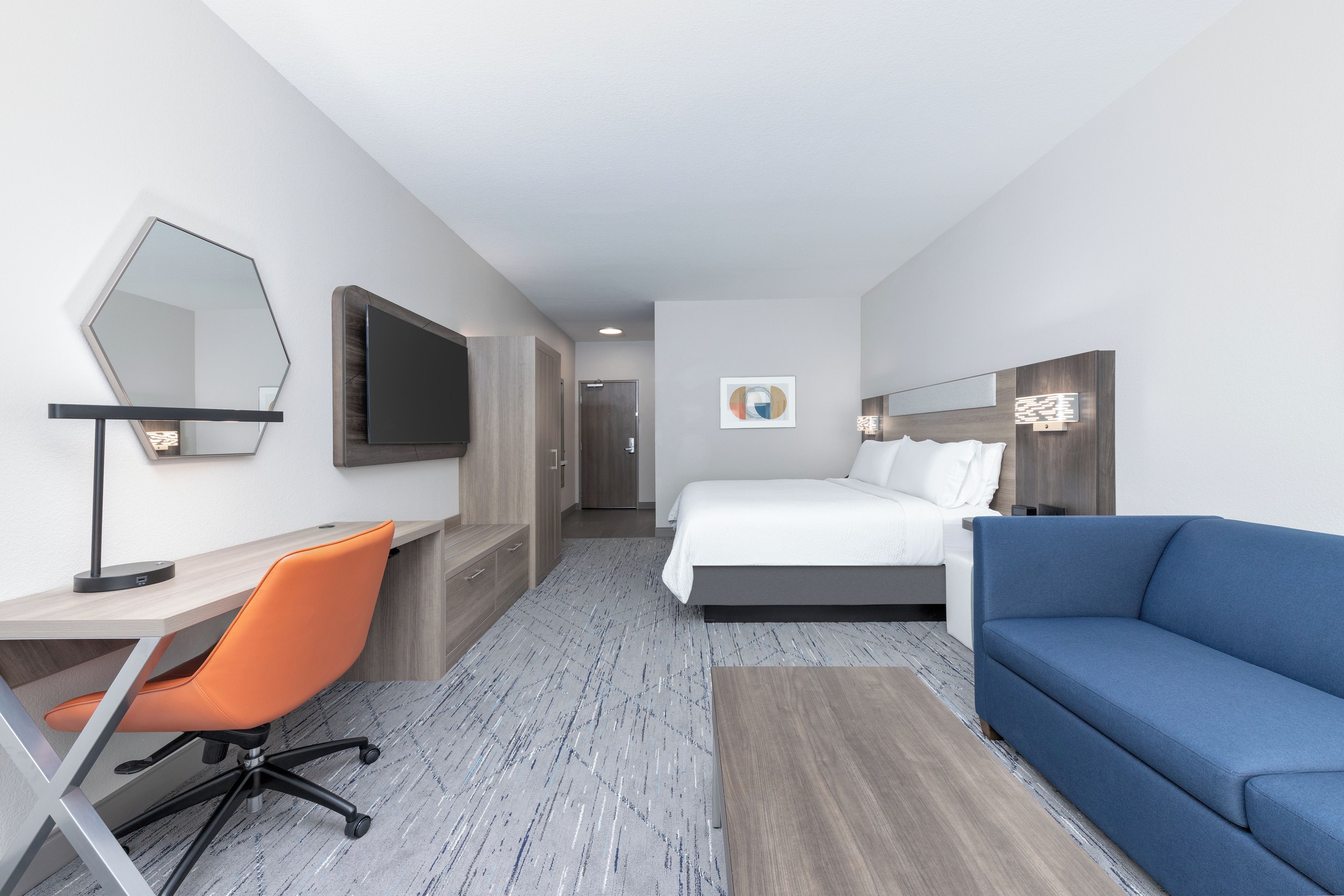 A hotel room with a bed, a desk with a chair, a TV, and a blue sofa.