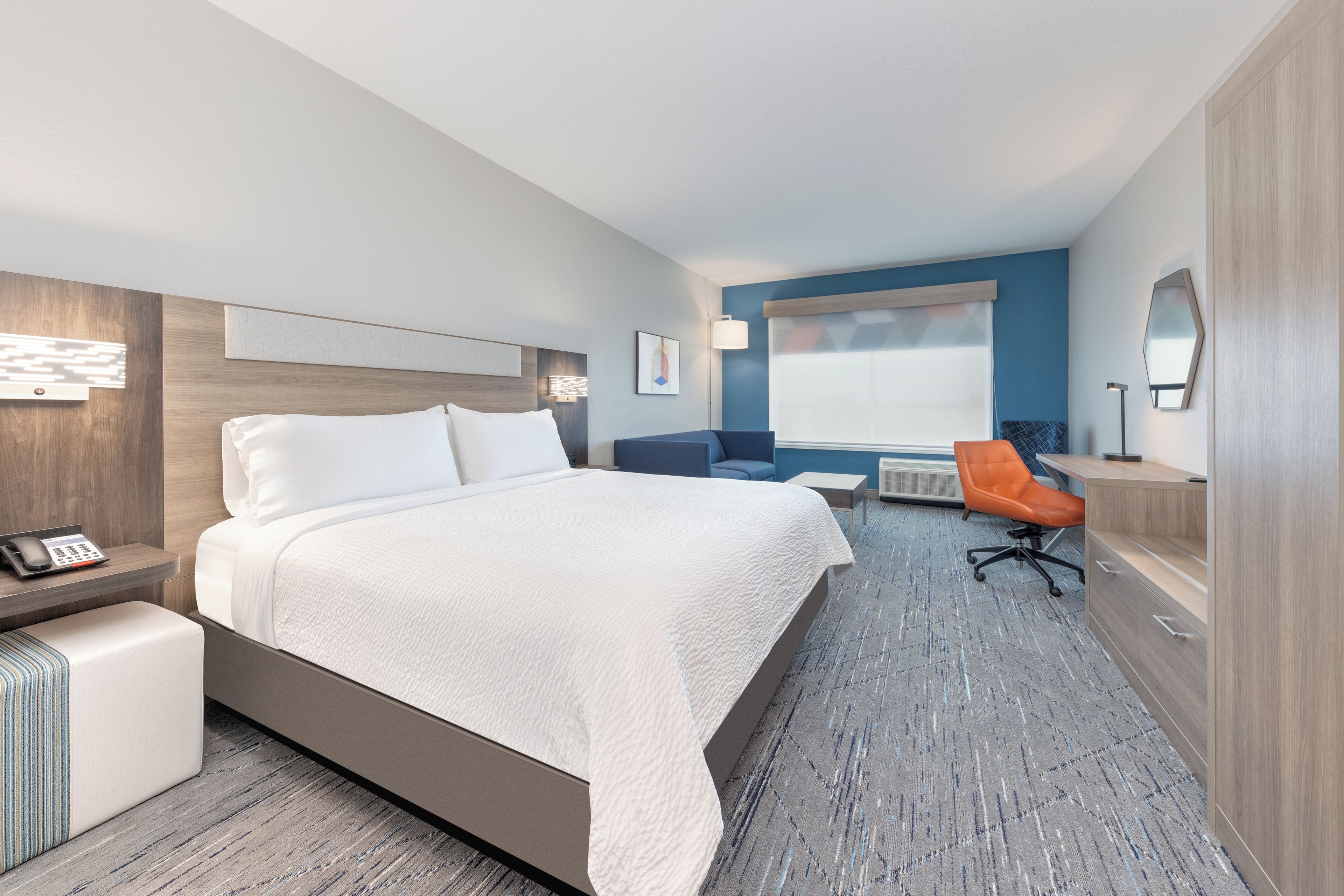 Una habitación de hotel con cama, escritorio, silla, ventana y espejo.