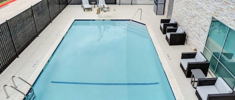 Una piscina rectangular con cercado metálico negro, sillas de descanso y un muro de piedra.