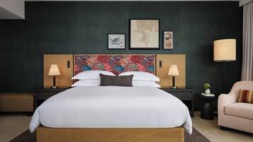 Una habitación de hotel con una cama grande, dos mesitas de noche con lámparas, un cabecero decorativo y una silla.