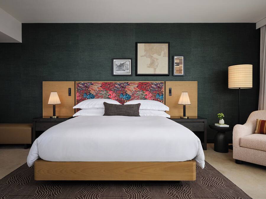 Una habitación de hotel con una cama grande, dos mesitas de noche con lámparas, un cabecero decorativo y una silla.